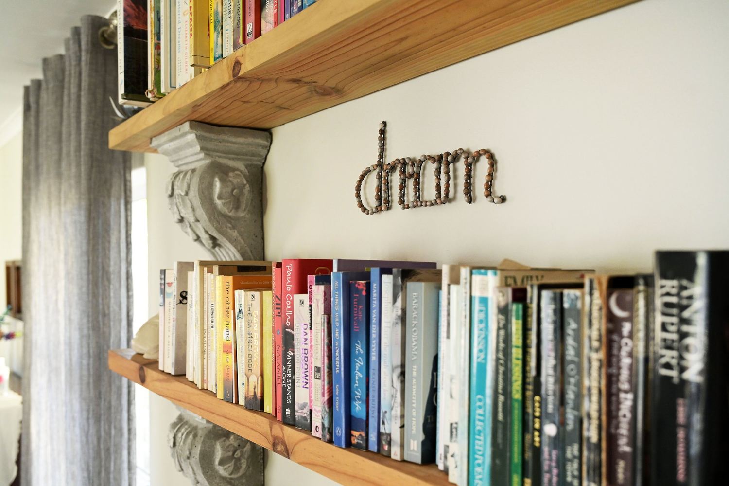 A bookshelf with the word Dream spelled in beads above rows of well-read books.
